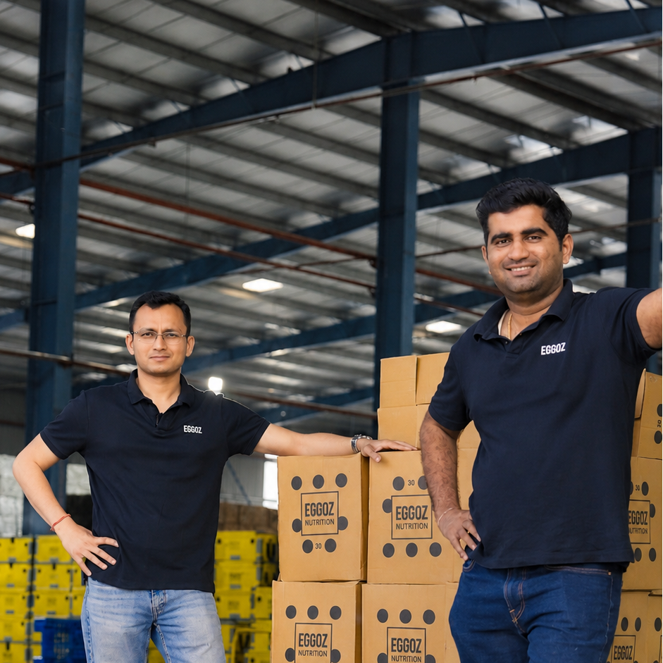Two men standing in a warehouse next to stacked cardboard boxes branded EGGOZ.